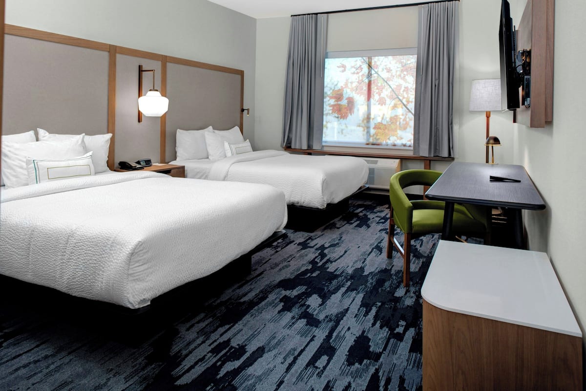 Een hotelkamer met twee bedden, een bureau, een stoel, een televisie en een raam met gordijnen.