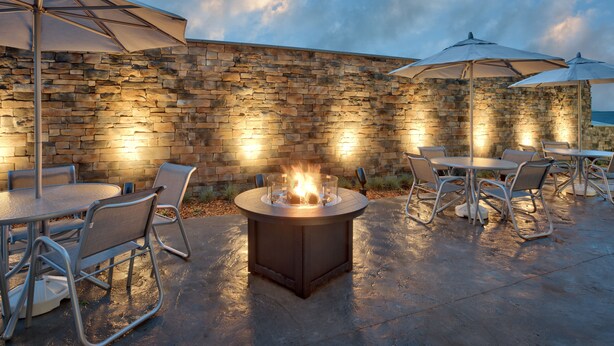 Une terrasse extérieure avec des murs en pierre, des tables rondes, des chaises et des parasols.
