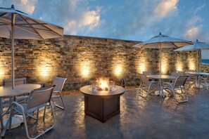 An outdoor patio with stone walls, round tables, chairs, and umbrellas. - Fairfield Inn & Suites by Marriott Springfield North (Springfield)