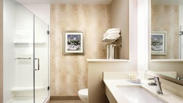 A modern bathroom with a glass shower enclosure, a toilet, a sink with a mirror, and a wall-mounted towel rack.