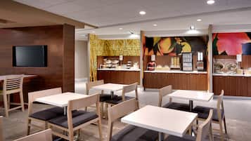 Interior moderno de restaurante com mesas e cadeiras de madeira, uma TV de tela plana na parede e um balcão com cardápio.