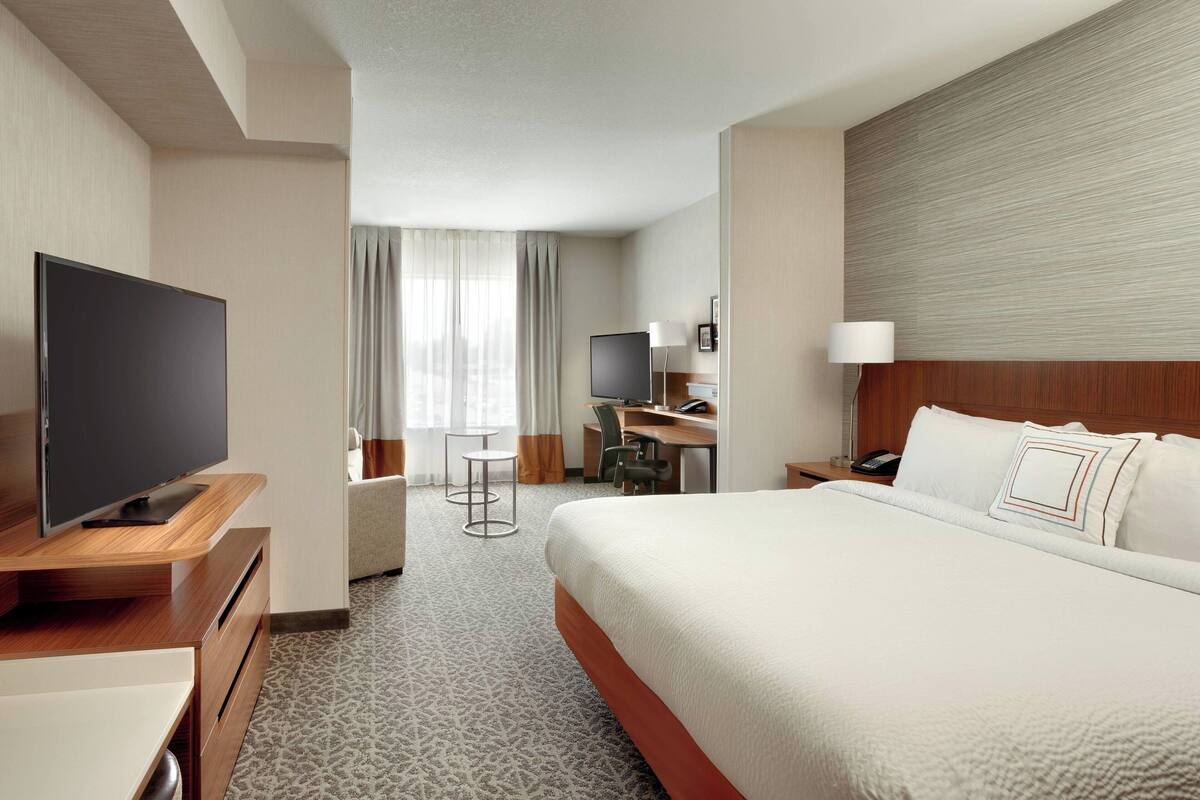 A hotel room with a large bed, a desk with a computer, a flat-screen TV, and a small seating area with a table and chairs.