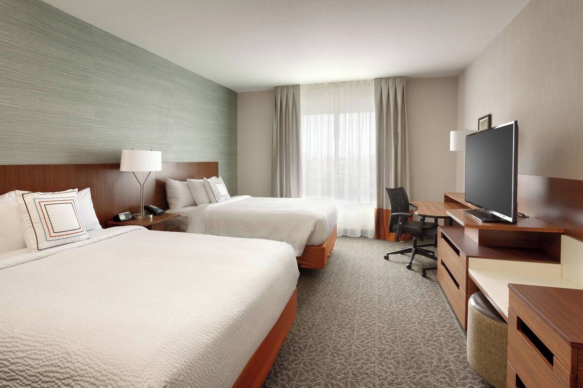 A hotel room with two beds, a desk with a computer, a TV, and a lamp.