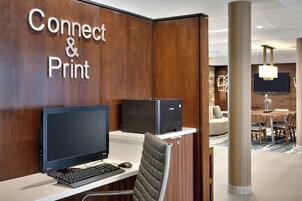 Un mostrador de recepción de hotel con una computadora, una impresora y una zona de estar con una mesa y sillas.