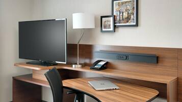 Een hotelkamer met een houten bureau, een flatscreen televisie, een lamp, een telefoon en een laptop.