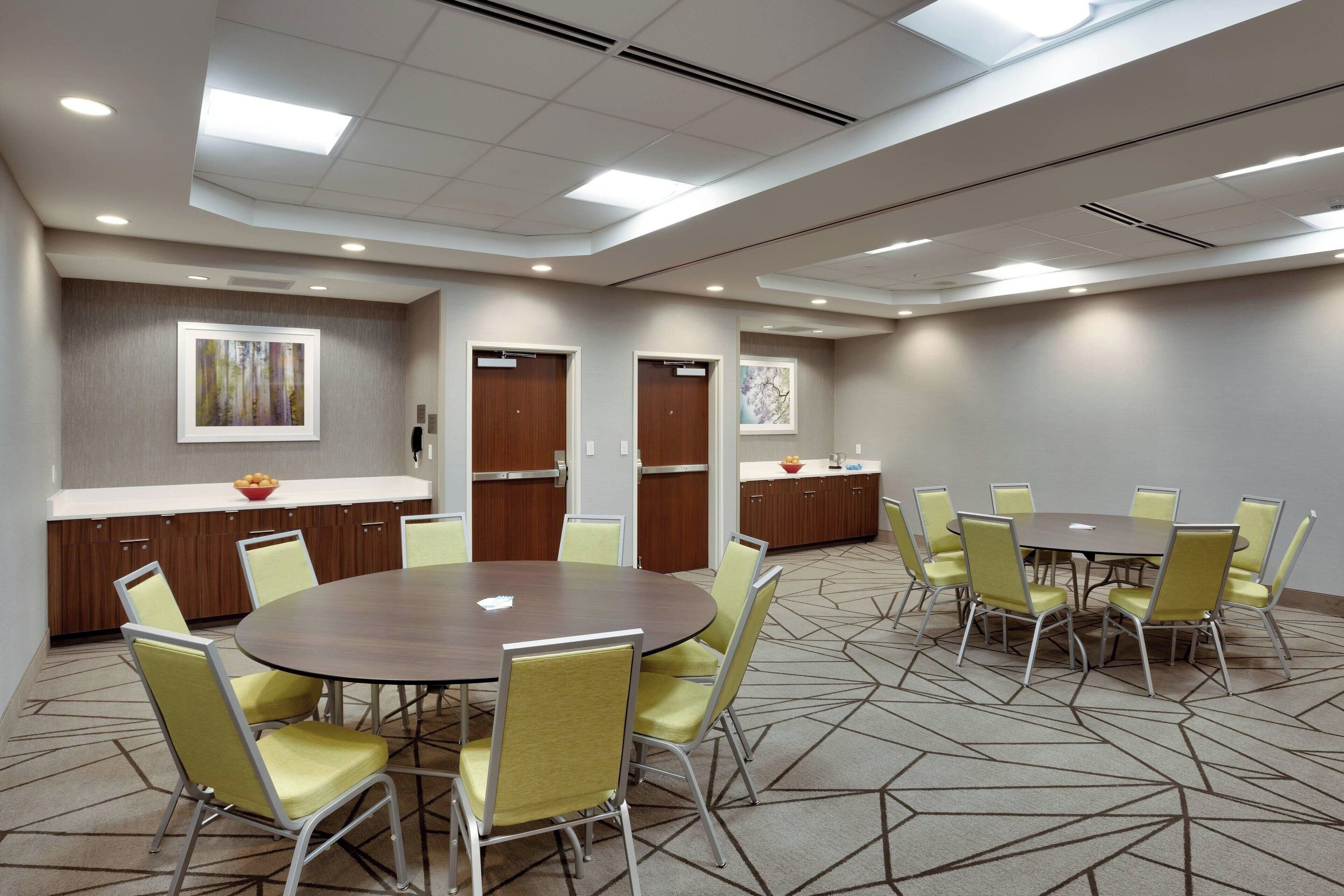 A conference room with a round table, yellow chairs, and a carpeted floor.