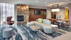 Une chambre d’hôtel moderne avec un mur d’accent en pierre, un téléviseur à écran plat, une cheminée, un canapé, un coin repas et une moquette à motifs.