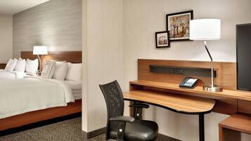 A hotel room with a bed, a desk, a chair, a lamp, a telephone, and a television.