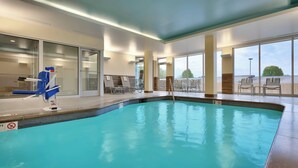 Une piscine intérieure avec des parois en verre transparent, des chaises longues et un poste de surveillance pour le sauveteur.