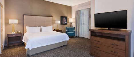 A hotel room with a large bed, two bedside tables with lamps, a flat-screen TV on a wooden stand, a ceiling fan, and a window with curtains.