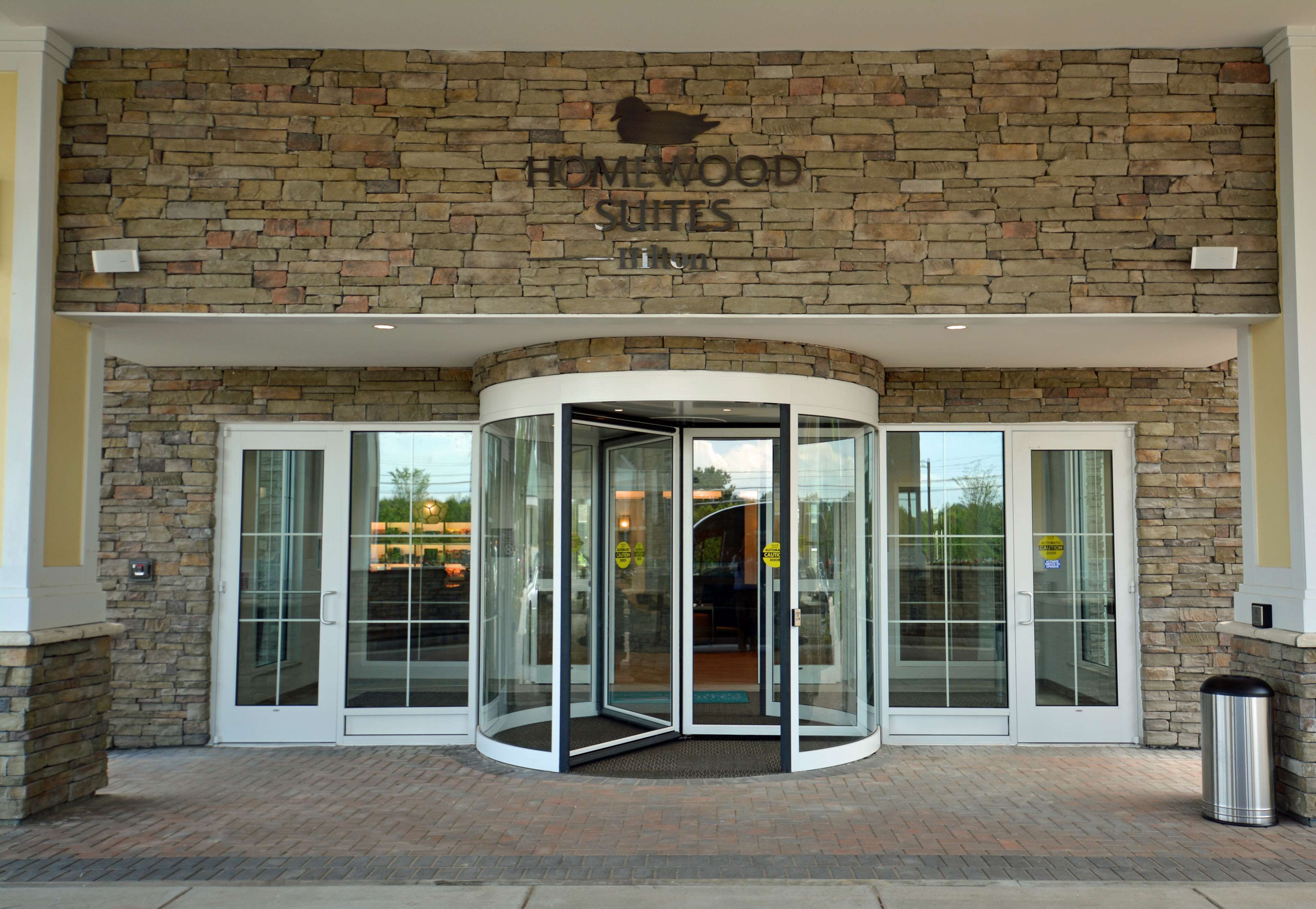 Entrada de un hotel con fachada de piedra, puerta giratoria y un letrero que dice "Homewood Suites Hilton".