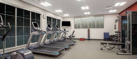 A gym with treadmills, weight machines, and a TV on the wall.