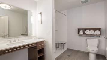 A modern bathroom with a large mirror, a sink with two faucets, a toilet, and a shower area.