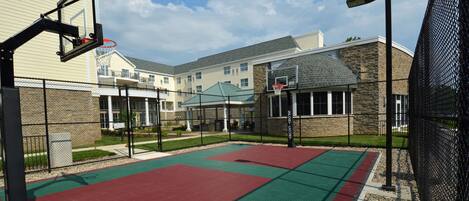 An outdoor basketball court with a red and green playing surface, surrounded by a chain-link fence.