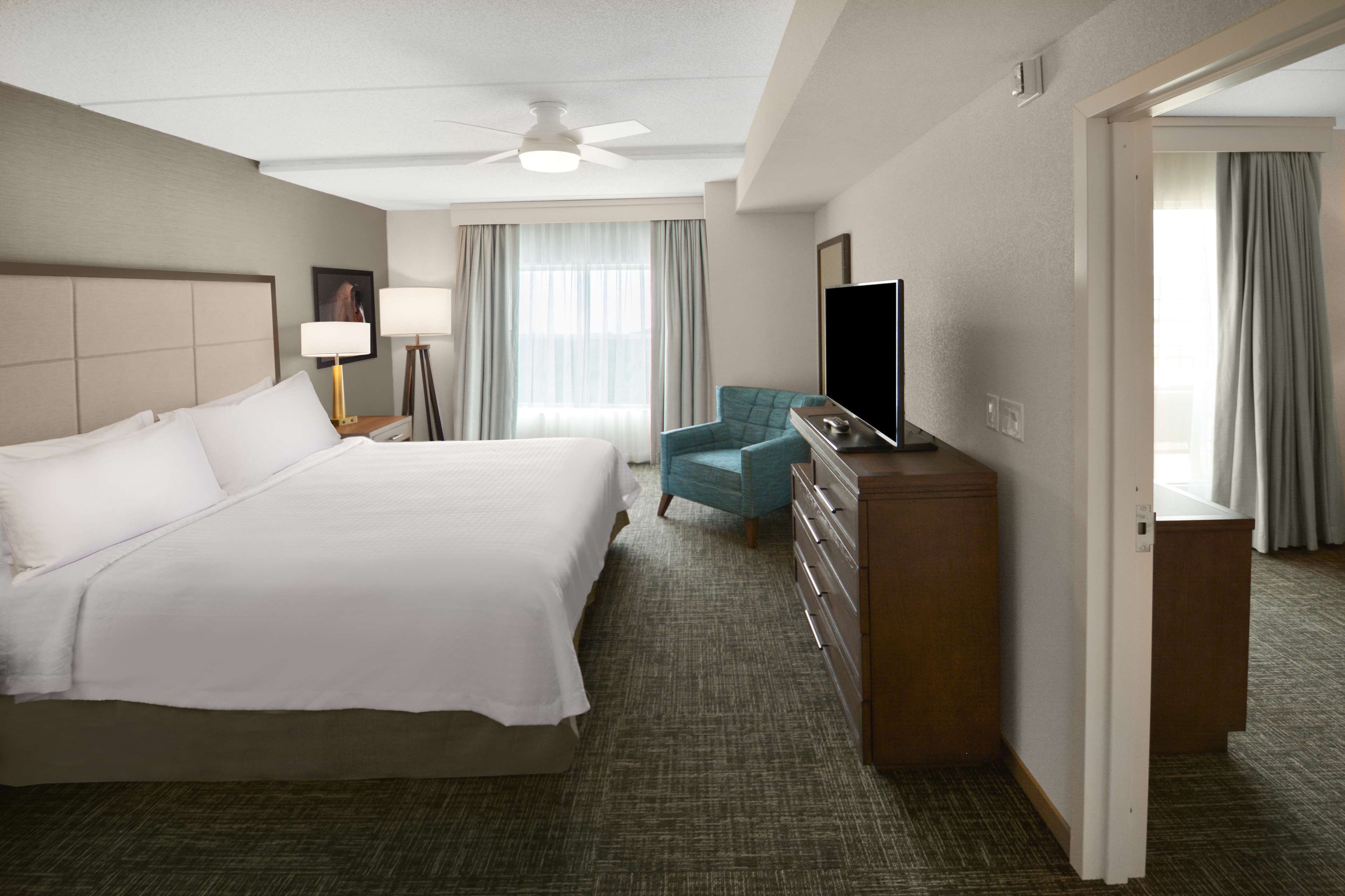 A hotel room with a large bed, a desk with a flat-screen TV, a chair, and a dresser.