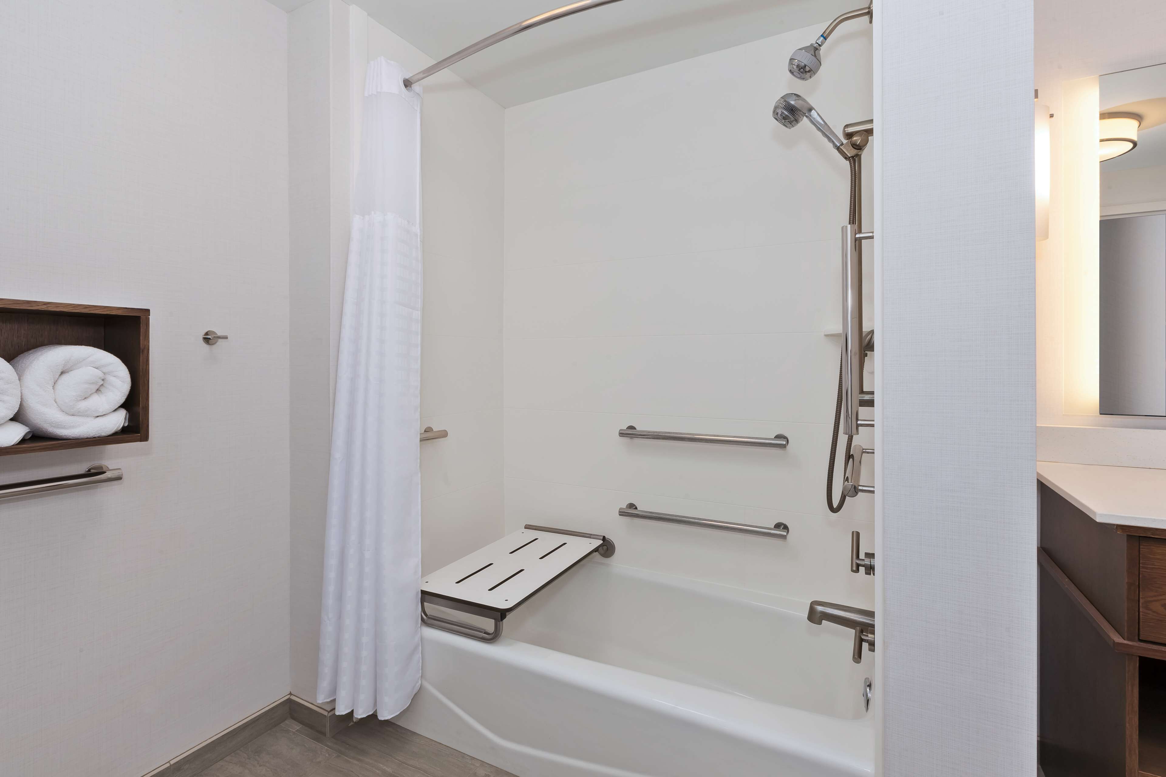 A modern bathroom with a walk-in shower, grab bars, and a towel rack.