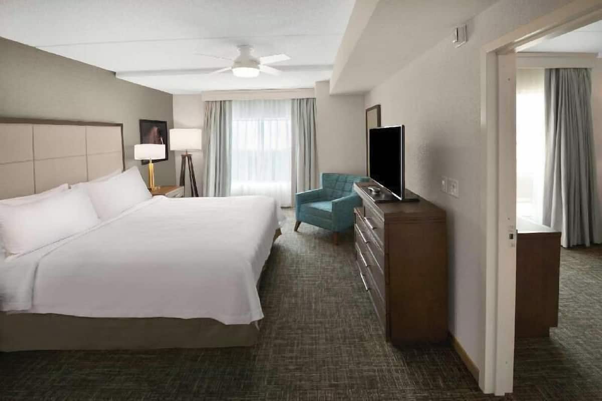 Quarto de hotel com cama, escrivaninha, cadeira, televisão e guarda-roupa.