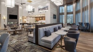 A modern hotel lobby with a bar area, seating arrangements, and large windows. - Homewood Suites by Hilton Saratoga Springs (Saratoga Springs)