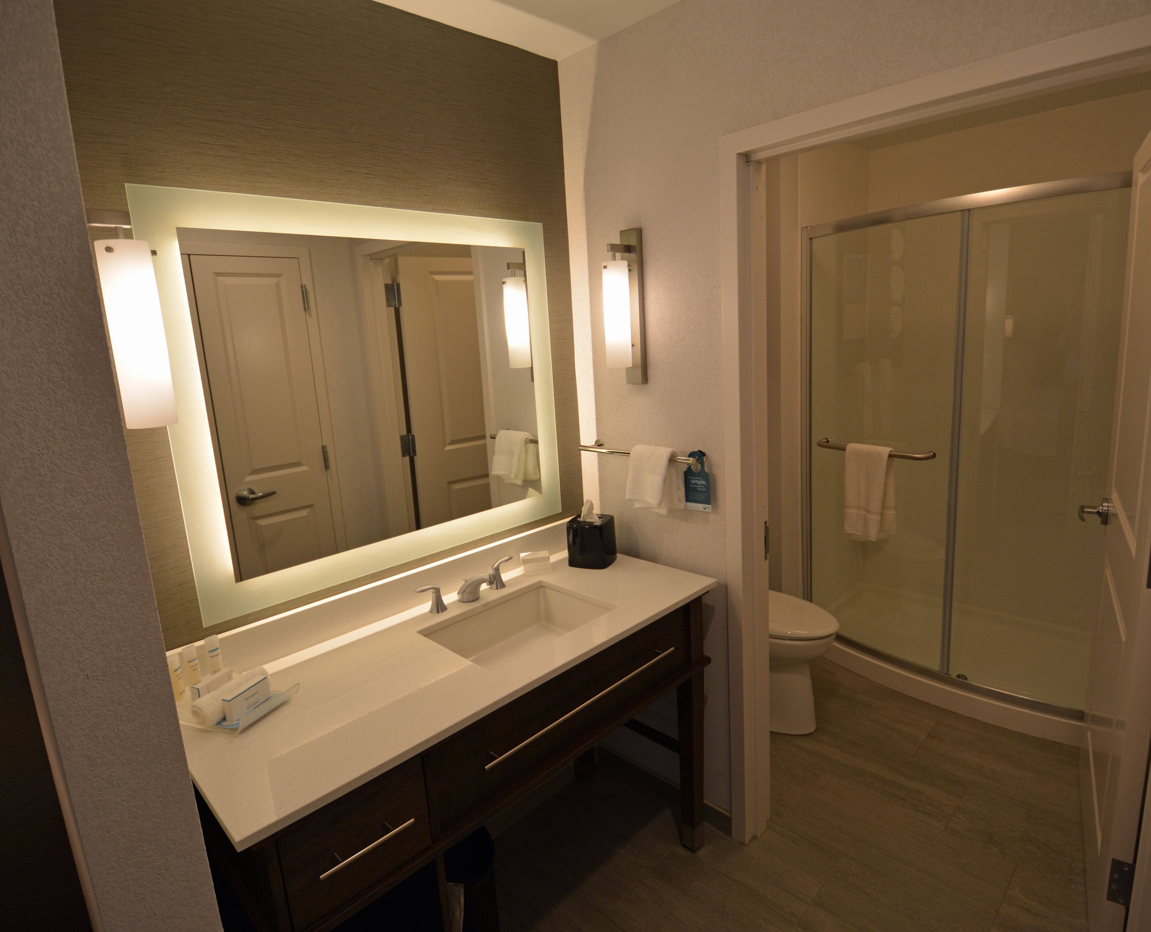 A modern bathroom with a large mirror, dual sinks, a toilet, and a glass-enclosed shower.