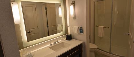 A modern bathroom with a large mirror, dual sinks, a toilet, and a glass-enclosed shower.