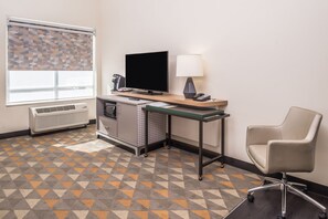A hotel room with a desk, chair, TV, lamp, air conditioning unit, and patterned carpet. - Holiday Inn Joplin by IHG (Joplin)