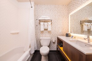 Une salle de bain moderne avec des toilettes blanches, une baignoire et un lavabo agrémenté d’un miroir.