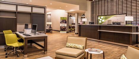 A hotel lobby with a reception desk, seating area, and a dining space.