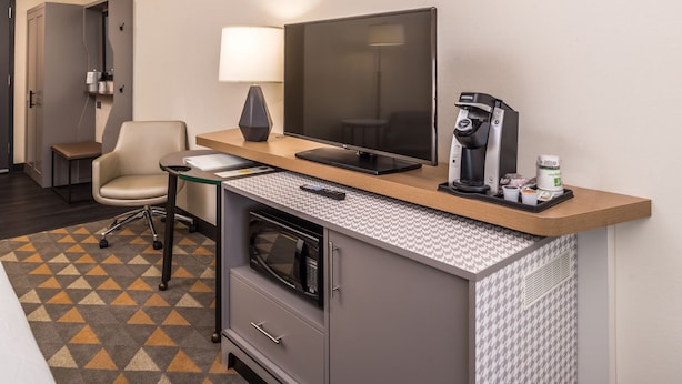 Ein Hotelzimmer mit Schreibtisch, Stuhl, Flachbildfernseher, Kaffeemaschine, Mikrowelle und einem gemusterten Teppich.