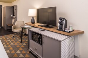 Une chambre d’hôtel équipée d’un bureau, d’une chaise, d’un téléviseur à écran plat, d’une machine à café, d’un four à micro-ondes et d’un tapis à motifs.