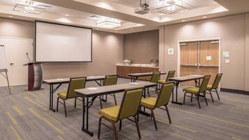 Un salón de conferencias con pantalla de proyector, mesas, sillas y un atril.