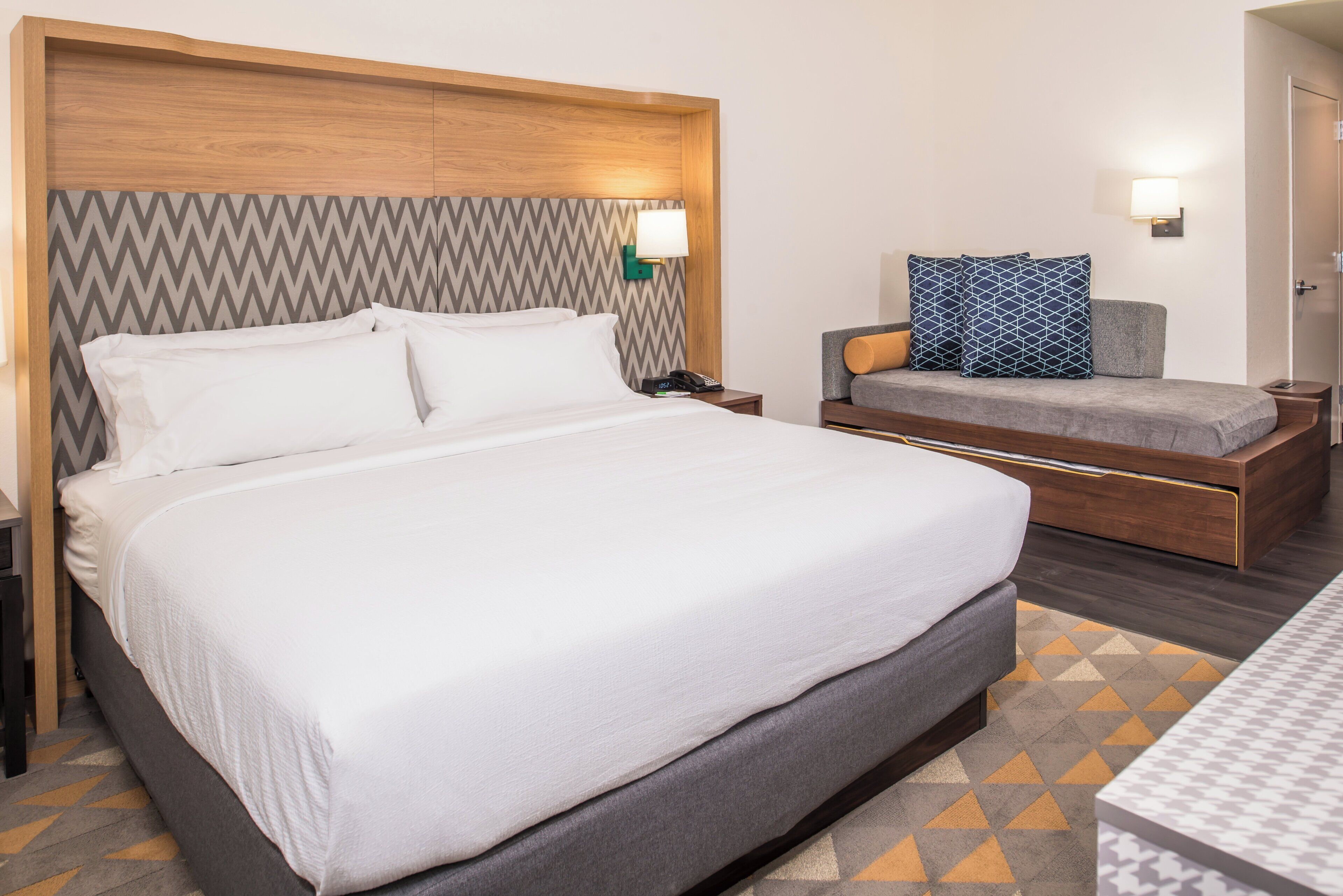 Una habitación de hotel con una cama grande, mesitas de noche, una silla y un escritorio.