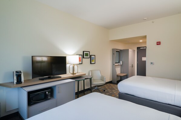 Une chambre d’hôtel comprenant un lit, un bureau avec une télévision, un four à micro-ondes, une chaise et une petite table.