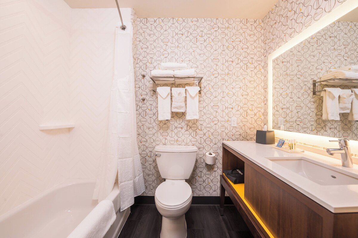 Une salle de bain moderne avec des toilettes blanches, une baignoire, un meuble-lavabo en bois et un miroir.