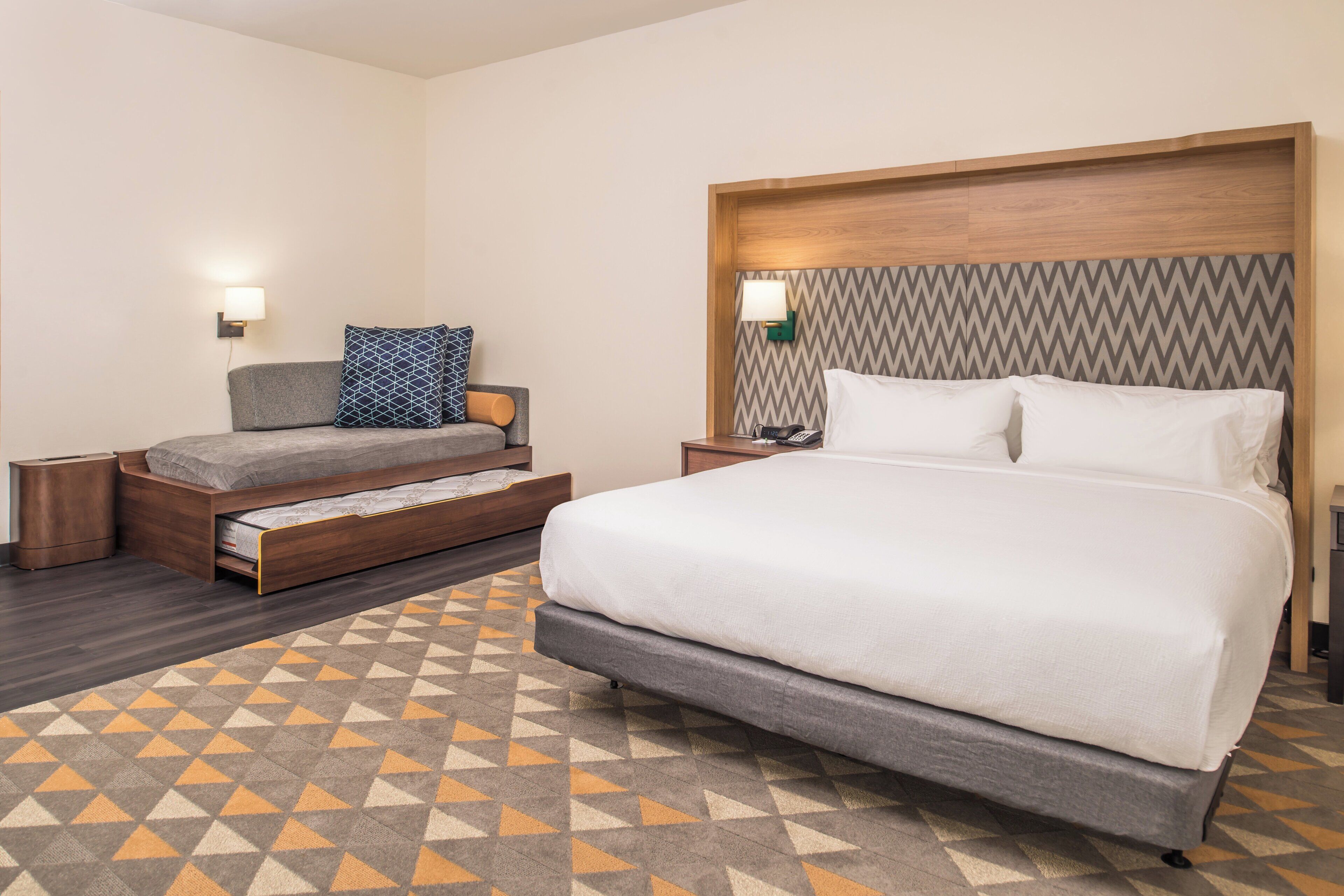 Une chambre d’hôtel comprenant un lit, un canapé-lit, une table de chevet avec une lampe et un tapis à motifs.
