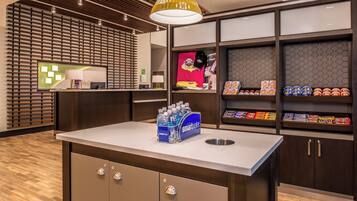 Ein Hotel-Rezeptionsbereich mit einer Theke, einem Wasserspender und Regalen voller Snacks.