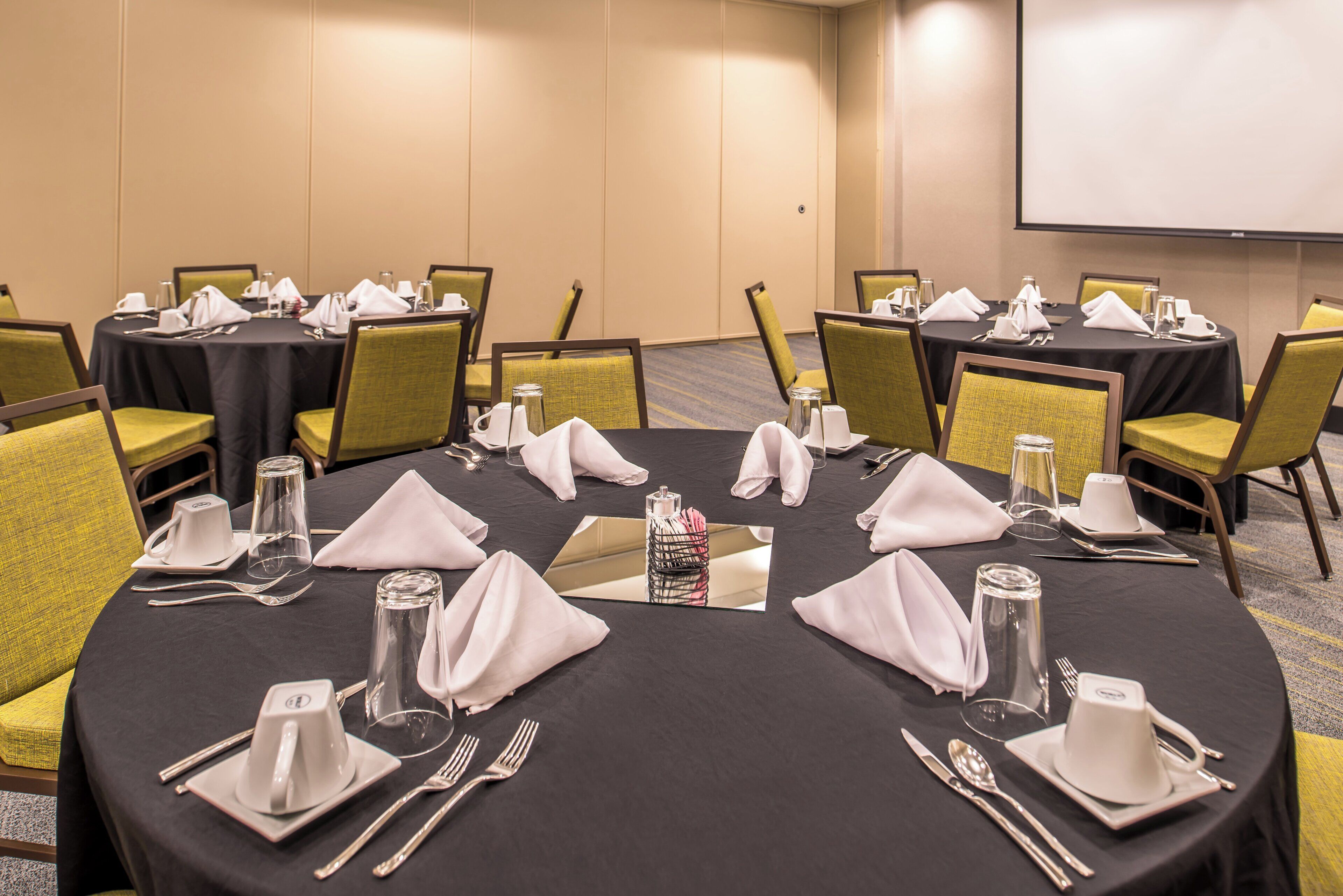 Un salón de conferencias con mesas redondas, sillas y mesas dispuestas con cubiertos y servilletas.