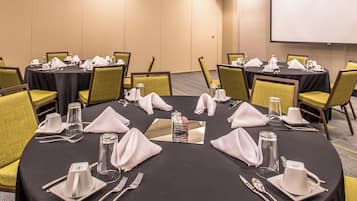 Un salón de conferencias con mesas redondas, sillas y mesas dispuestas con cubiertos y servilletas.