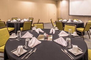 A conference room with round tables, chairs, and neatly set dining tables with cutlery and napkins.