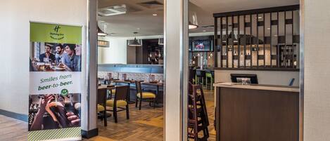 A hotel lobby with a reception desk, a bar area, and a seating area with tables and chairs.