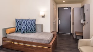 Ein modernes Hotelzimmer mit einem hölzernen Bett, einer Bank, einer Wandleuchte und einer Tür zu einem Badezimmer.