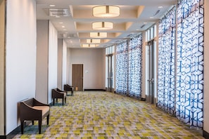 A hotel corridor with patterned carpet, modern lighting, and a view through large windows.