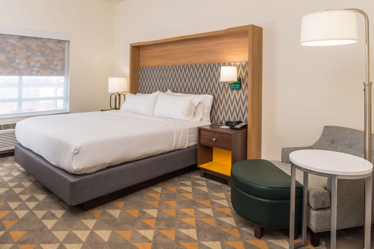 A hotel room with a bed, bedside table, lamp, chair, and a small table.