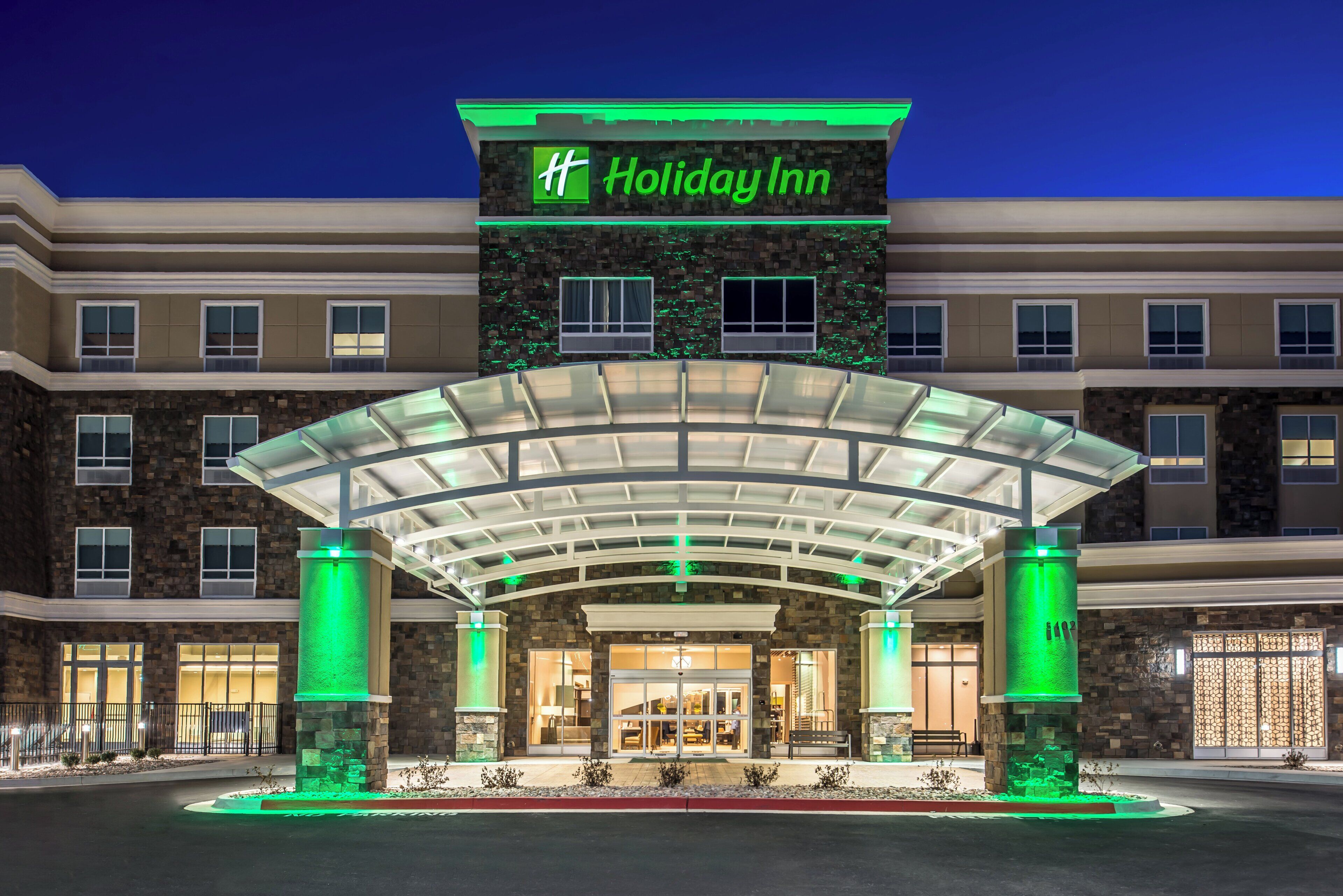 Een Holiday Inn hotel met een overdekte ingang, een gevel van natuursteen en verlichte signage.