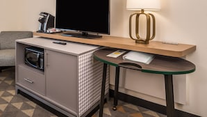 Ein kompaktes Hotelzimmer mit Küchenzeile, einem Flachbildfernseher, einer Lampe und einem kleinen Tisch.