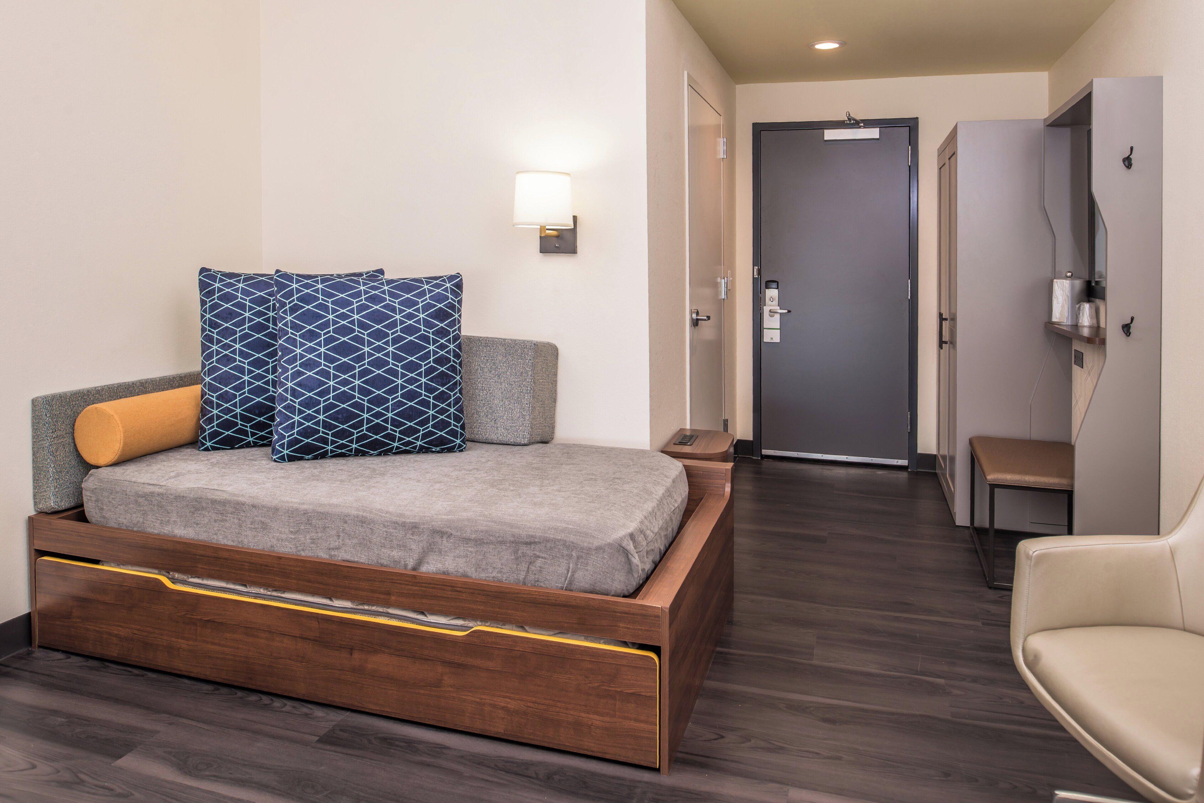 A modern hotel room with a bed, bedside table, lamp, and a chair.