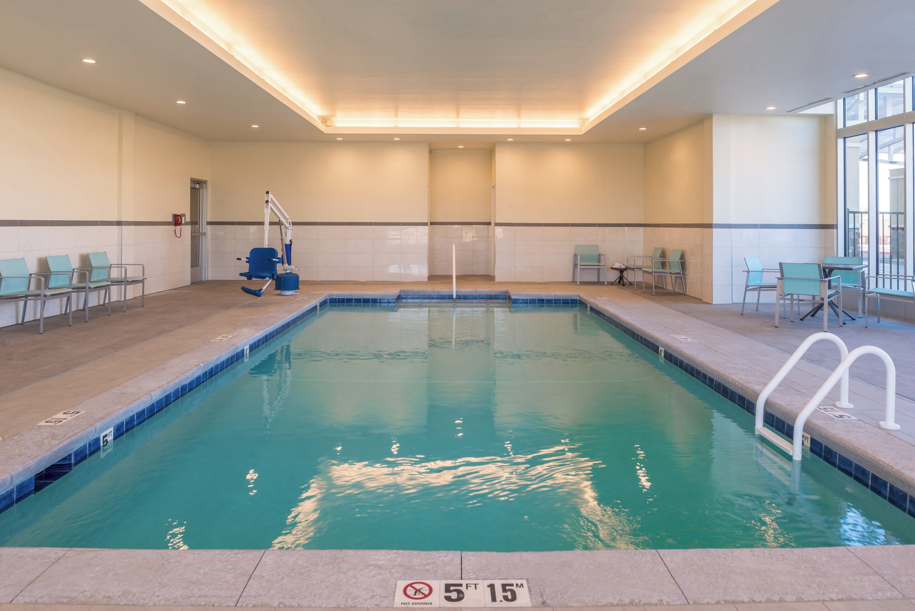An indoor swimming pool with a no diving sign, chairs, and a changing room.
