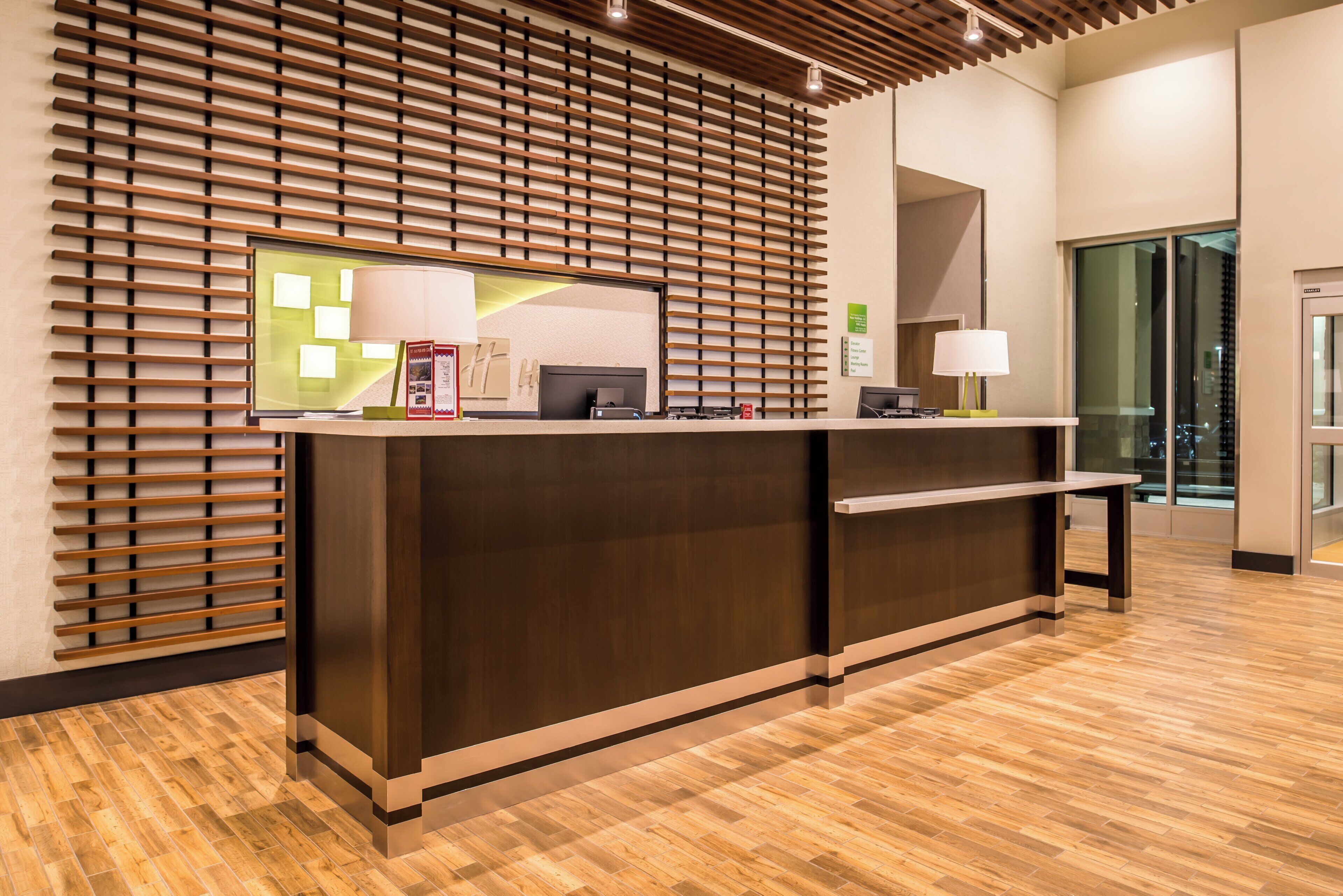 A reception desk with a wooden slat design, a computer, and a lamp.