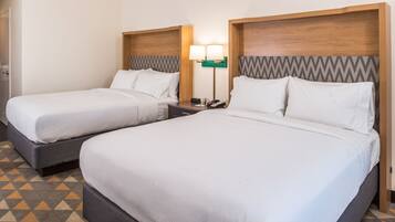 A hotel room with two beds, a nightstand, a lamp, and a patterned floor.
