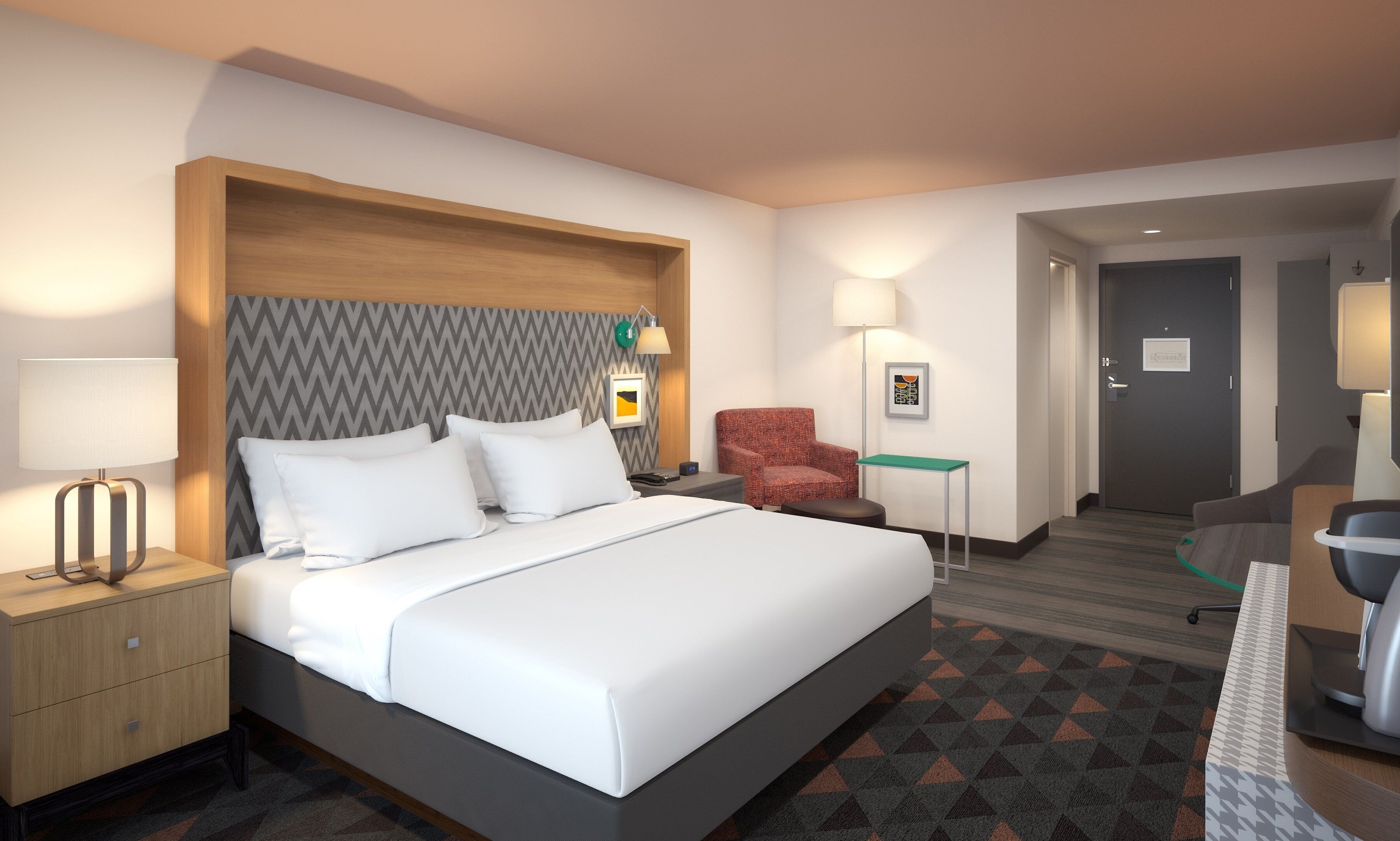 Una habitación de hotel con cama, mesita de noche, lámpara, silla, escritorio y una puerta que da a otra habitación.