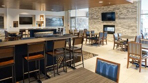 A modern hotel lobby with a bar area, seating arrangements, and a stone wall with a fireplace. - Holiday Inn Express & Suites Denver - Aurora Medical Campus by IHG (Aurora)